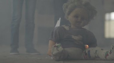 Arka planda duman bulutu içinde karanlık odada iki erkek bacakları. Korkunç kirli bebek ön planda yerde yanıyor. Yangın kavramı, yanıcılık, güvenlik kurallarına uyulmaması