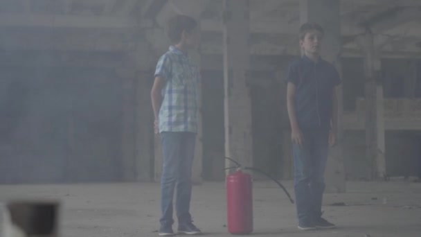 Zwei kleine Jungen stehen im dunklen, verrauchten Raum und schauen auf einen Feuerlöscher. Konzept des Feuers, der Entflammbarkeit, der Nichteinhaltung von Sicherheitsvorschriften — Stockvideo