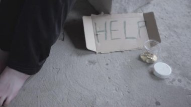 Terk edilmiş binada tozlu bir boşta oturan tanınmayan yalınayak zavallı kızın ayakları. Yardım ve kavanoz yazan ve yanında bozuk paralar olan bir tabela. Evsiz bayanın yardıma ihtiyacı var..