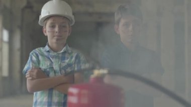 Kirli yüzleri ve koruyucu kasklı iki küçük çocuk yangın söndürücüye bakıyor. Yangın kavramı, yanıcılık, güvenlik kurallarına uyulmaması.