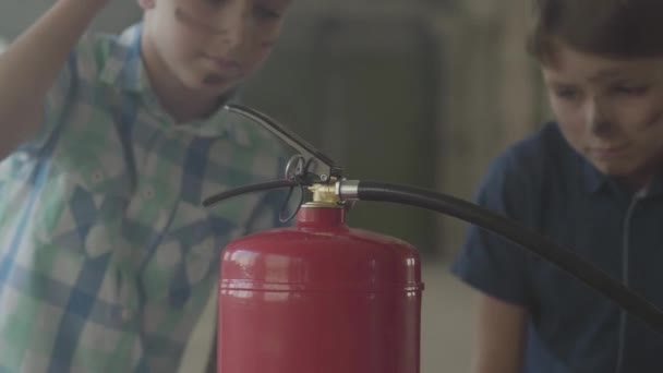 Two little boys with dirty faces and in protective helmets looking at the fire extinguisher with interest. Concept of fire, flammability, non-compliance with safety rules — Stock Video