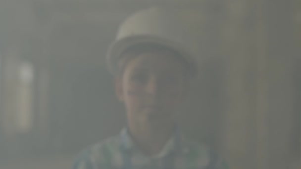 Ritratto teen boy in un casco protettivo guardando la fotocamera sullo sfondo di fumo all'interno. Concetto di incendio, disastro, infiammabilità, inosservanza delle norme di sicurezza . — Video Stock