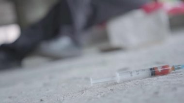 Beton zeminde kan la birlikte şırınga kullanılmış. Arka planda sallanan keşin bulanık figürü. Uyuşturucu bağımlılığı