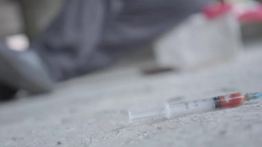 Beton zeminde kan la şırınganın yakın çekim. Arka planda sallanan keşin bulanık figürü. Uyuşturucu bağımlılığı.