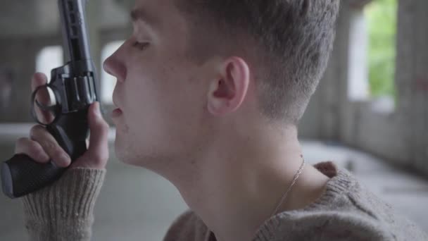 Side view of a depressed crazy young man holding revolver in hands, slowly blowing out cigarette smoke in abandoned building. The guy going to commit suicide or kill human — Stock Video