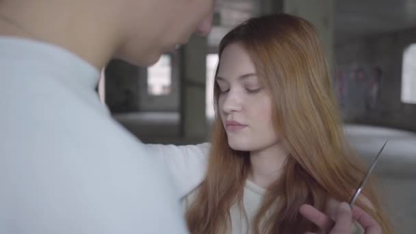 Jeune homme mettant un couteau au cou d'une belle fille aux cheveux roux et menace sur le fond d'un bâtiment abandonné .