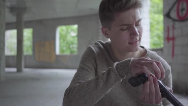 Joven hombre despreocupado carga el revólver cantando una canción de cerca. El tipo que se prepara para matar humanos poniendo balas en el arma en un edificio abandonado. Brutalidad de los adolescentes — Vídeos de Stock