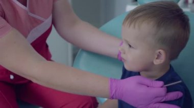 Diş hekimi diş ofisinde sandalyede oturan küçük tasasız çocuk dişlerini kontrol etmeye hazır. Kadın profesyonel doktor stomatoloji uzmanı iş başında. Diş tedavisi, tıbbi kavram.