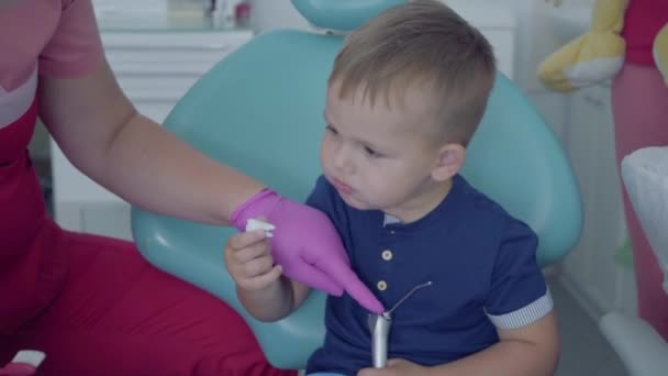 Sandalyede oturan az kaygısız çocuk. Diş implantıyla oynayan sevimli çocuk. Kadın profesyonel doktor stomatoloji uzmanı iş başında. Diş tedavisi, tıbbi konsept. Diş bakımı. — Stok video