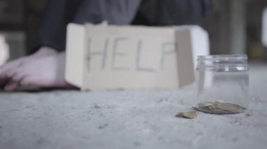 Evsiz erkek ya da kadın bir karton işareti yardım ve yardım ve yardım için para için kavanoz ile terk edilmiş bir binada oturan. Close.
