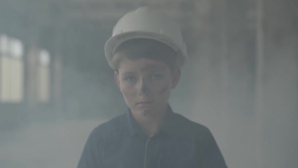 Retrato de niño en un casco protector saliendo de un pilar de humo y mirando a la cámara. Concepto de incendio, catástrofe, inflamabilidad, incumplimiento de las normas de seguridad — Vídeos de Stock