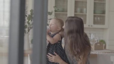 Güzel gülümseyen genç kadın mutfakta bebek şişesinden nasıl içilir onu bebek kız gösteren. Mutlu bir aile, bir çocuk, annelik, aşk kavramı. Yavaş çekim