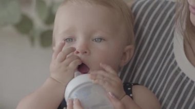 Yakın çekim güzel bir kız bebek mutfakta yardım ile küçük bebek şişesinden su içme. Mutlu bir aile, bir çocuk, annelik, aşk kavramı. Yavaş çekim