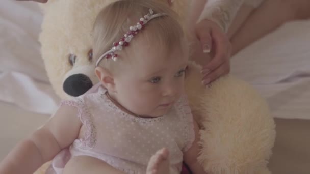 Kleine baby meisje in een roze jurk liggend op de beer speelgoed thuis terwijl de handen van haar moeder borstelen haar haren met Childrens borstel. Concept van een gelukkige familie, een kind, liefde. Slow Motion — Stockvideo