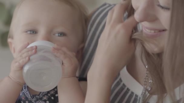 Close-up bonito jovem mulher alimentando sua menina a partir da pequena mamadeira na cozinha. Conceito de uma família feliz, um filho, maternidade, amor. Movimento lento — Vídeo de Stock