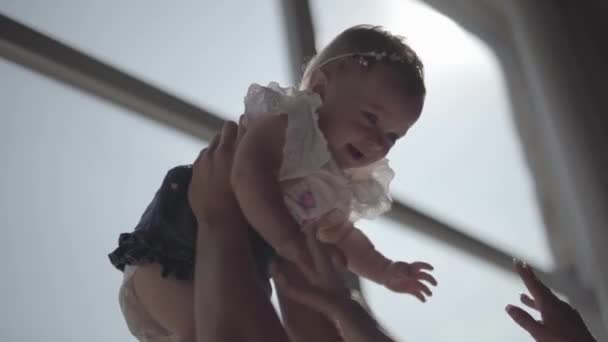 Primeros planos de las manos de la mujer levantando a su niña sonriente delante de una gran ventana. La madre jugando con su hijo en casa. Concepto de una familia feliz, un niño, amor — Vídeos de Stock