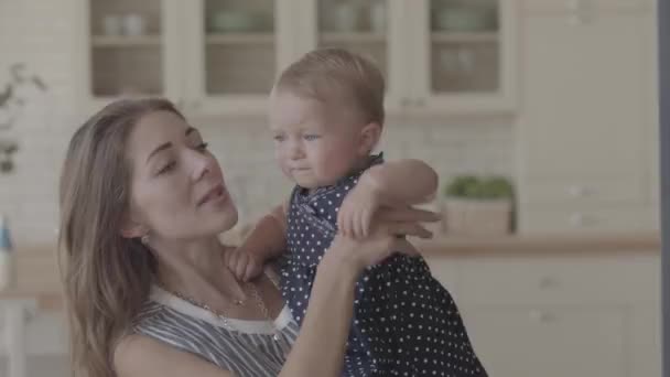 Close-up portret van een mooie moeder en schattige baby binnenshuis samen. Kaukasische moeder houdt een baby in haar armen thuis. — Stockvideo