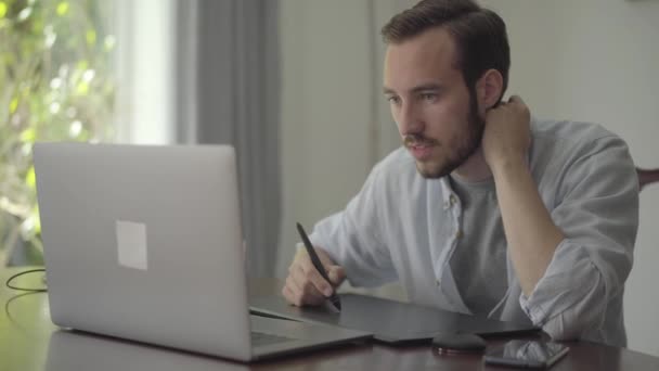 Der erfolgreiche bärtige Kerl zeichnet mit einem Grafiktablett, das in einen Laptop blickt. männliche Handzeichnung 3D Animation Produktion Modellierung Design modernes Coworking Studio. Serie "echte Menschen". — Stockvideo