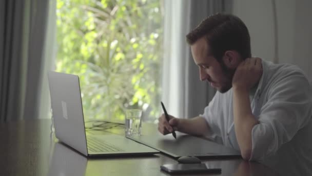 Fiducioso uomo barbuto disegna utilizzando tablet grafico guardando in un computer portatile. Disegno a mano maschio 3d animazione produzione modellazione design moderno coworking studio . — Video Stock