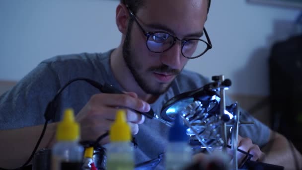 Portrait d'un jeune homme barbu à succès dans des lunettes travaillant avec un fer à souder à son lieu de travail. Concept de la profession, travail précis, poste d'ingénieur — Video