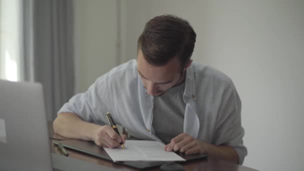 テーブルに座っている男が家で紙に何かを書いている。職業概念、作家、コピーライター、編集者。リアルピープルシリーズ. — ストック動画