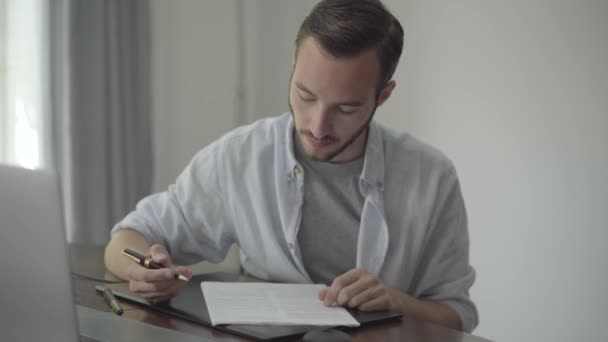 Der junge Schriftsteller, der am Tisch sitzt und seinen Essay korrigiert, schreibt mit schwarzem und goldenem Stift auf das Papier und zeigt den Daumen nach oben. Berufskonzept, Schriftsteller, Werbetexter, Redakteur. Serie "echte Menschen". — Stockvideo