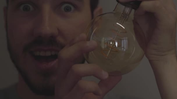 Primer plano del hombre barbudo sonriente atornillar y apagar una bombilla en el fondo oscuro. Concepto de luz y oscuridad, idea, electricidad en el hogar moderno. Serie de personas reales . — Vídeos de Stock