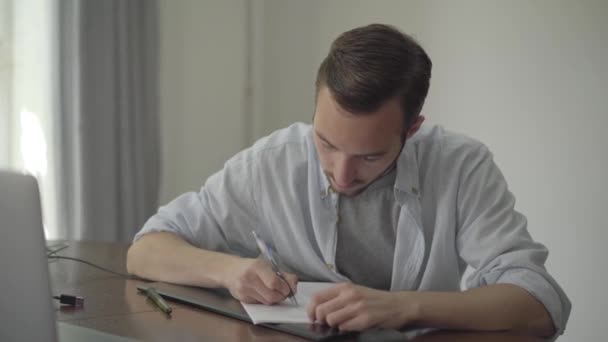 Muž, který sedí u stolu a píše něco na papíře doma. Profesní koncepce, spisovatel, copywriter, redaktor. Série skutečných lidí. — Stock video