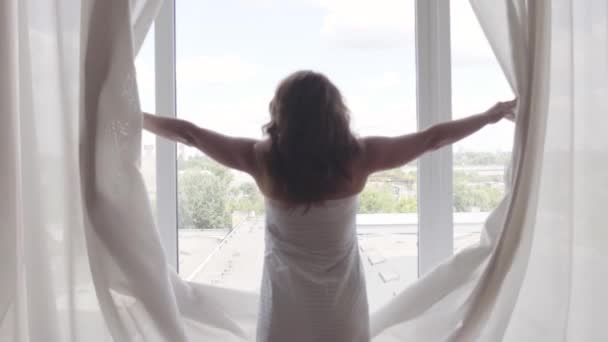 Rear back view at rich mature woman opening curtain lace standing in luxury apartment home or modern hotel looking through window enjoying wellbeing. Happy caucasian woman greets new day. — Stock Video