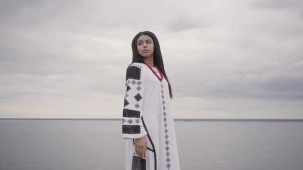 Achteruitkijk bij ontzag Afro-Amerikaanse vrouw dragen lange zomer mode jurk staande op het veld op de achtergrond van een meer of rivier. Schattig African American Girl uitgaven vrije tijd buitenshuis. — Stockvideo