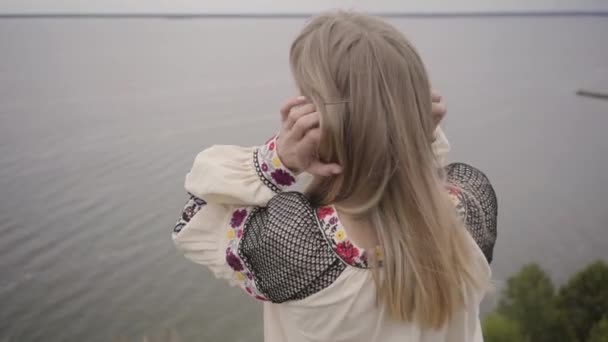 Vista trasera a la mujer caucásica despreocupada con vestido largo de moda de verano de pie en el campo en el fondo de un lago o río. Linda chica afroamericana pasar tiempo libre al aire libre . — Vídeo de stock