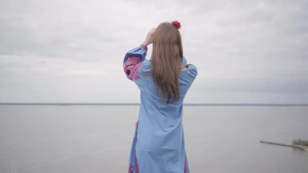 Заднього виду на безтурботна кавказька жінка носить довге Літнє плаття мода стоячи на полі на тлі озера або річки. Симпатичні афро-американські дівчата витрачають дозвілля на відкритому повітрі. — стокове відео