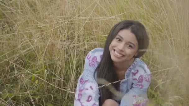 Retrato encantador seguro de sí mismo despreocupado niña afroamericana con vestido de moda de verano largo disfrutando sentado en el campo. Mujer joven mirando a la cámara al aire libre. Serie de personas reales . — Vídeo de stock