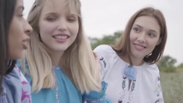 Vista de cerca de tres novias en vestidos de verano con bordado sentado y hablando en el campo. Concepto de moda, conexión con la naturaleza, vida rural, amistad — Vídeos de Stock