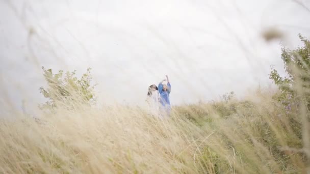 Tre flickvänner i vackra långa sommar klänningar med broderi hoppning i fältet går genom fältet. Mode, samband med natur, landsbygdsliv, vänskap — Stockvideo