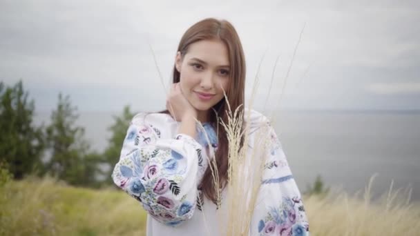 Portret charmant zelfverzekerd zorgeloos Kaukasische meisje dragen lange zomer mode jurk genieten van het kijken naar de camera. Vrije tijd en weekend van een mooie jonge vrouw die een bos gras buiten houdt. — Stockvideo