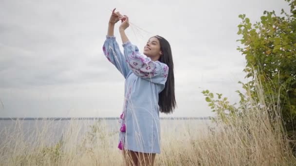 Retrato de la hermosa joven afroamericana en vestido corto con bordado sosteniendo un montón de hierba seca en el campo. Concepto de moda, conexión con la naturaleza, estilo de vida rural — Vídeos de Stock