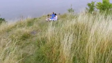 Göl veya nehir yakınında oturan uzun yaz moda elbise giyen üç kız hava görünümü. İki Beyaz ve bir Afro-Amerikan kız boş zamanlarını dışarıda geçiriyorlar. Drone çekim.