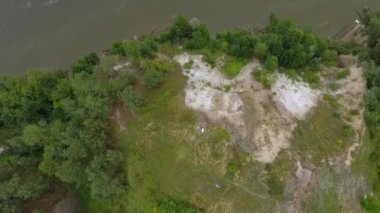 Nehirdeki yüksek bir tepede dans eden ve dönen üç kız arkadaşın havadan görüntüsü. Doğayla bağlantı, kırsal yaşam, dostluk. İnsansız hava aracı atışı, en iyi görüntü. Kamera aşağı hareket ediyor