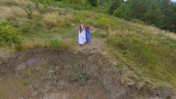 Flygvy på tre flickvänner bär lång sommar mode klänning promenad nära sjön eller floden. Två kaukasiska och en afroamerikanska flickor spenderar fritid utomhus. Drone skytte. — Stockvideo