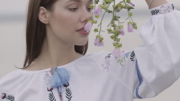 Portret charmant zorgeloos meisje dragen lange zomer mode jurk op zoek naar vertrouwen bij camera genieten van stands op het veld. Vrije tijd van een mooie jonge vrouw die een bloeiende Wildflower buitenshuis vasthoudt. — Stockvideo