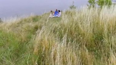 Göl veya nehir yakınında oturan uzun yaz moda elbise giyen üç kız hava görünümü. İki Beyaz ve bir Afro-Amerikan kız boş zamanlarını dışarıda geçiriyorlar. Drone çekim.