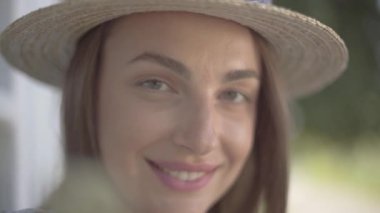 Hasır şapkalı çekici genç kadının yakın çekim portresi kameraya bakarak mutlu bir şekilde açık havada gülümsüyor. Duygu, kırsal yaşam tarzı, doğal güzellik kavramı