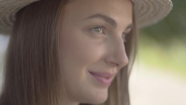 Nahaufnahme Porträt einer attraktiven jungen Frau mit Strohhut, die wegschaut und in die Kamera lächelt. Emotionen, ländlicher Lebensstil, natürliches Schönheitskonzept — Stockvideo