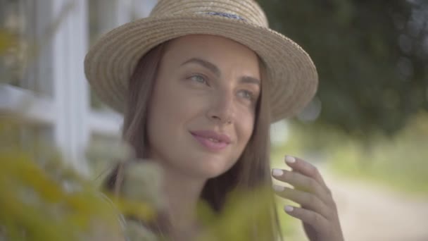 Cara de cerca de la atractiva joven con sombrero de paja mirando hacia otro lado sonriendo al aire libre. Emoción, estilo de vida rural, concepto de belleza natural . — Vídeo de stock