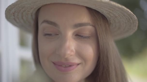 Hasır şapkalı sevimli genç kadının yakın çekim yüzü kameraya bakarak mutlu bir şekilde açık havada gülümsüyor. Duygu, kırsal yaşam tarzı, doğal güzellik kavramı — Stok video
