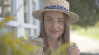 Hasır şapkalı sevimli genç kadının yakın çekim yüzü kameraya bakarak mutlu bir şekilde açık havada gülümsüyor. Duygu, kırsal yaşam tarzı, doğal güzellik kavramı