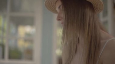 Yakın çekim bir hasır şapka ve beyaz elbise li genç kırsal kız kitap okuma açık havada küçük ahşap masada oturan. Kırsal yaşam tarzı. Güzel bir yaz gününde boş zaman. Yavaş çekim.