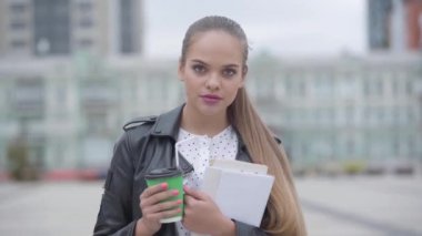 Kapuçino veya espresso fincan ile oldukça güven mutlu kız Portresi şehrin arka planda kamera bakarak sabahın erken saatlerinde ayakta. Gerçek insanlar serisi. Yavaş çekim