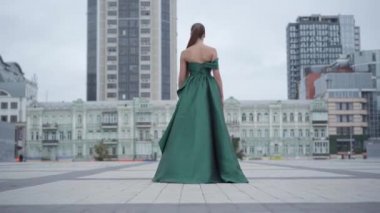 Muhteşem bir akşam yeşili elbise ile muhteşem kız geri görünümü gökdelen yakınındaki boş şehir meydanında büyüleyici yürüyüş. Gerçek insanlar serisi.